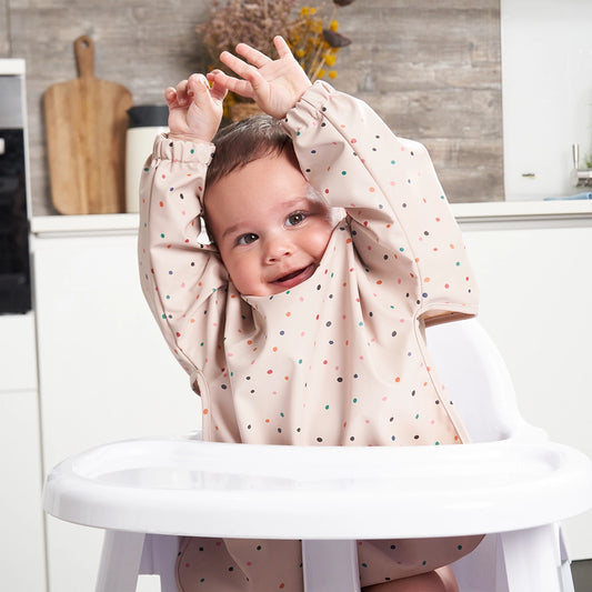 Baby Playing in Their Highchair Ready for Lunch, Wearing a Long Sleeved Bib in Light Pink or Orange Colour