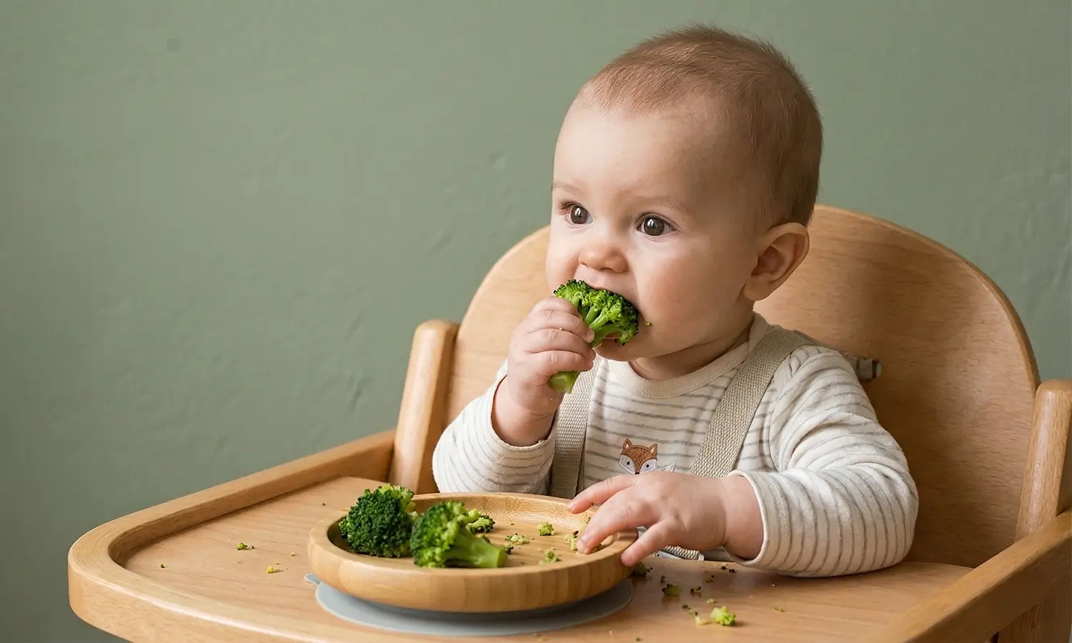Baby reaching for a broccoli floret during their first solids session