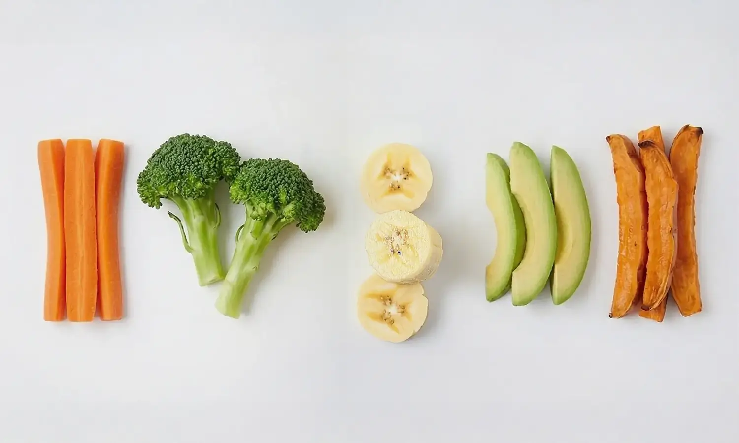 Bâtonnets de carotte, fleurettes de brocoli, rondelles de banane, tranches d'avocat et patate douce rôtie, sélection de premiers aliments pour la diversification de bébé